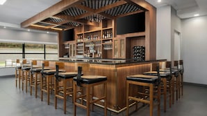 A bar area with wooden bar stools and a counter stocked with bottles and glasses.