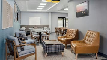A modern hotel lobby with a seating area, a dining table, and a large window.