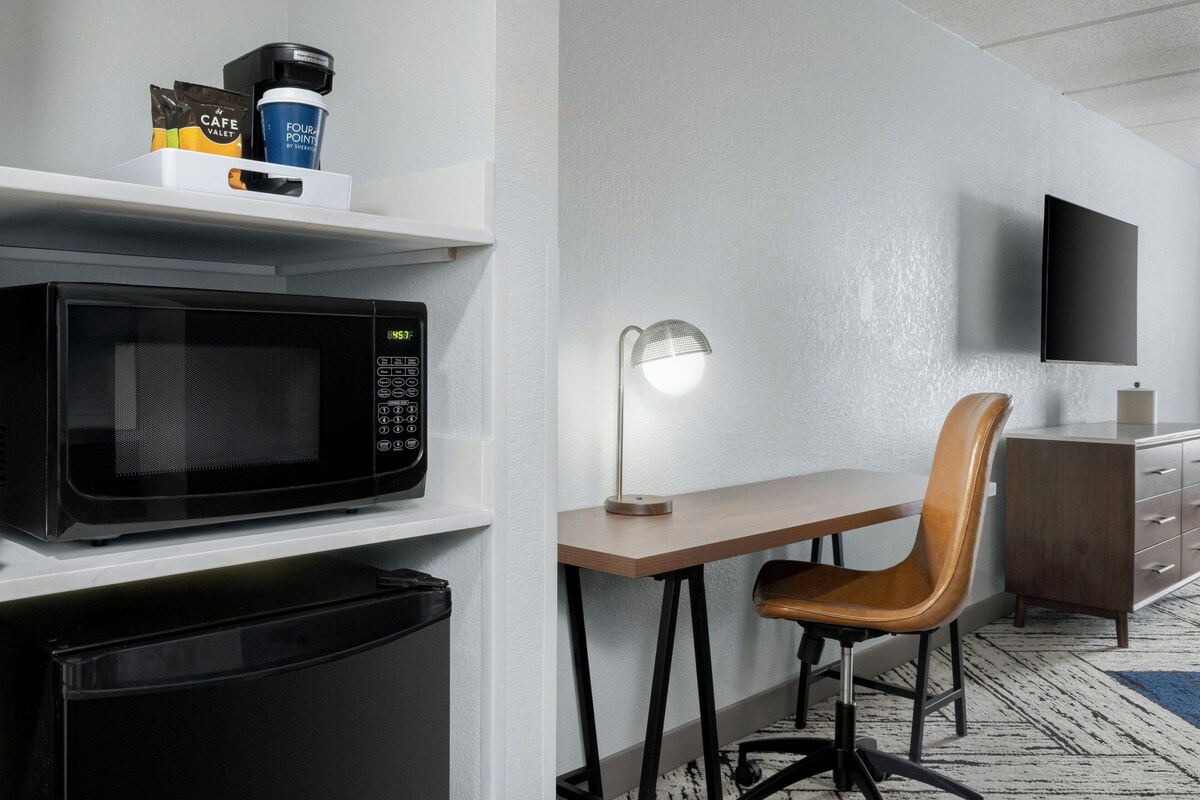 Een kleine hotelkamer met een magnetron, koffiezetapparaat en een bureau met stoel.