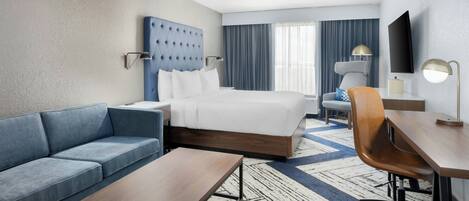 A hotel room with a bed, a sofa, a desk, and a TV.