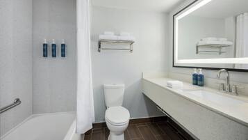 A modern bathroom with a white toilet, a bathtub, a sink with a mirror, and a towel rack.