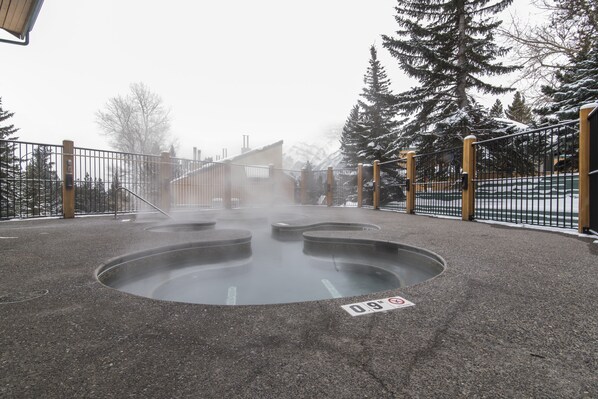 A hot spring area with a circular pool, surrounded by a fence and trees. - Douglas Fir Resort and Chalets (Banff)