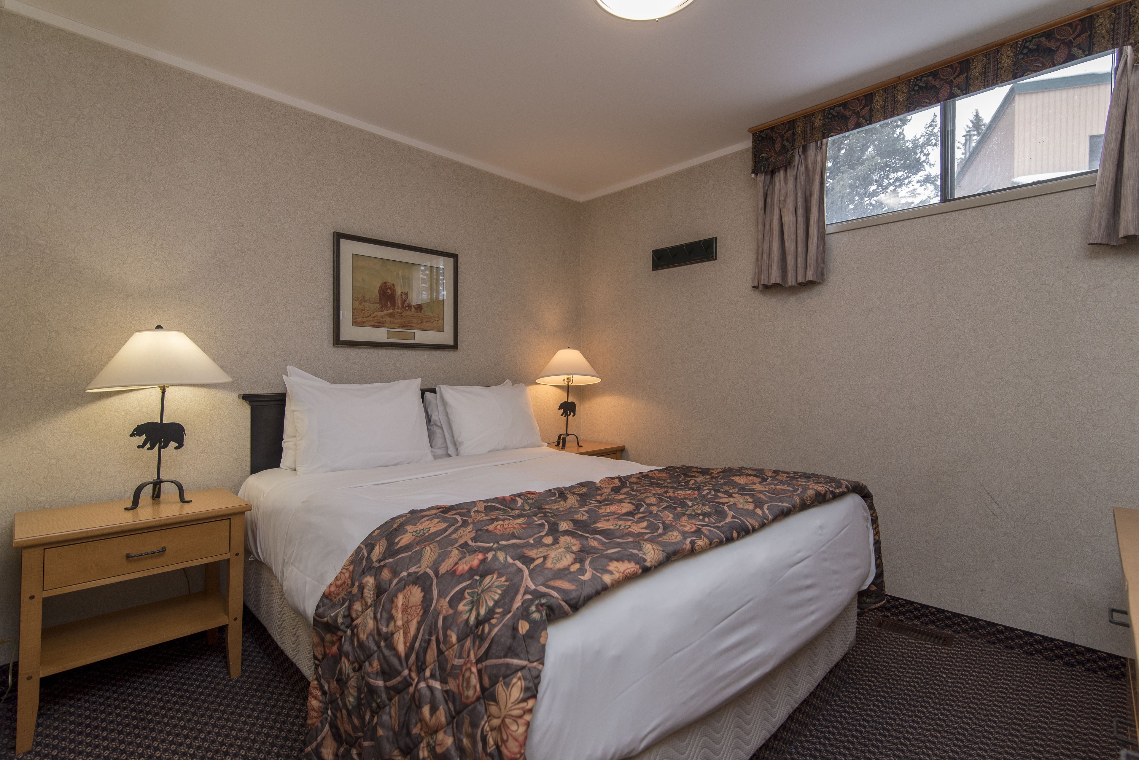 A hotel room with a large bed, two bedside lamps, a nightstand with a lamp, a framed picture on the wall, and a window with curtains.