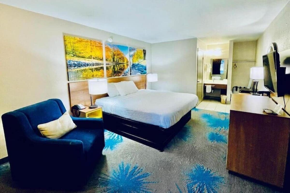 A hotel room with a bed, a chair, a desk, and a painting on the wall.