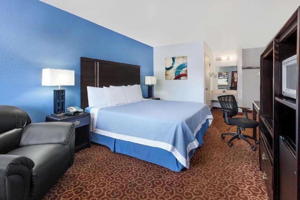 A hotel room with a bed, a desk, a chair, a TV, and a lamp.