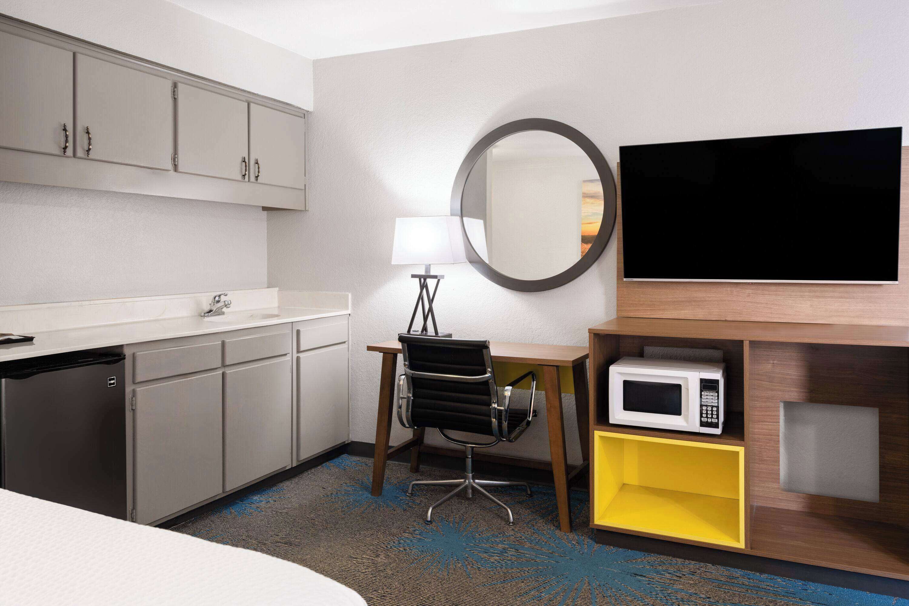 A hotel room with a bed, a desk with a chair, a microwave, a TV, and a small cabinet.