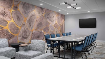 Un salón de conferencias con una mesa grande, sillas azules, sofás grises y una pared con textura de madera.