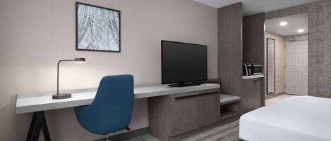 A hotel room with a bed, a desk with a chair, a television, and a framed picture on the wall.