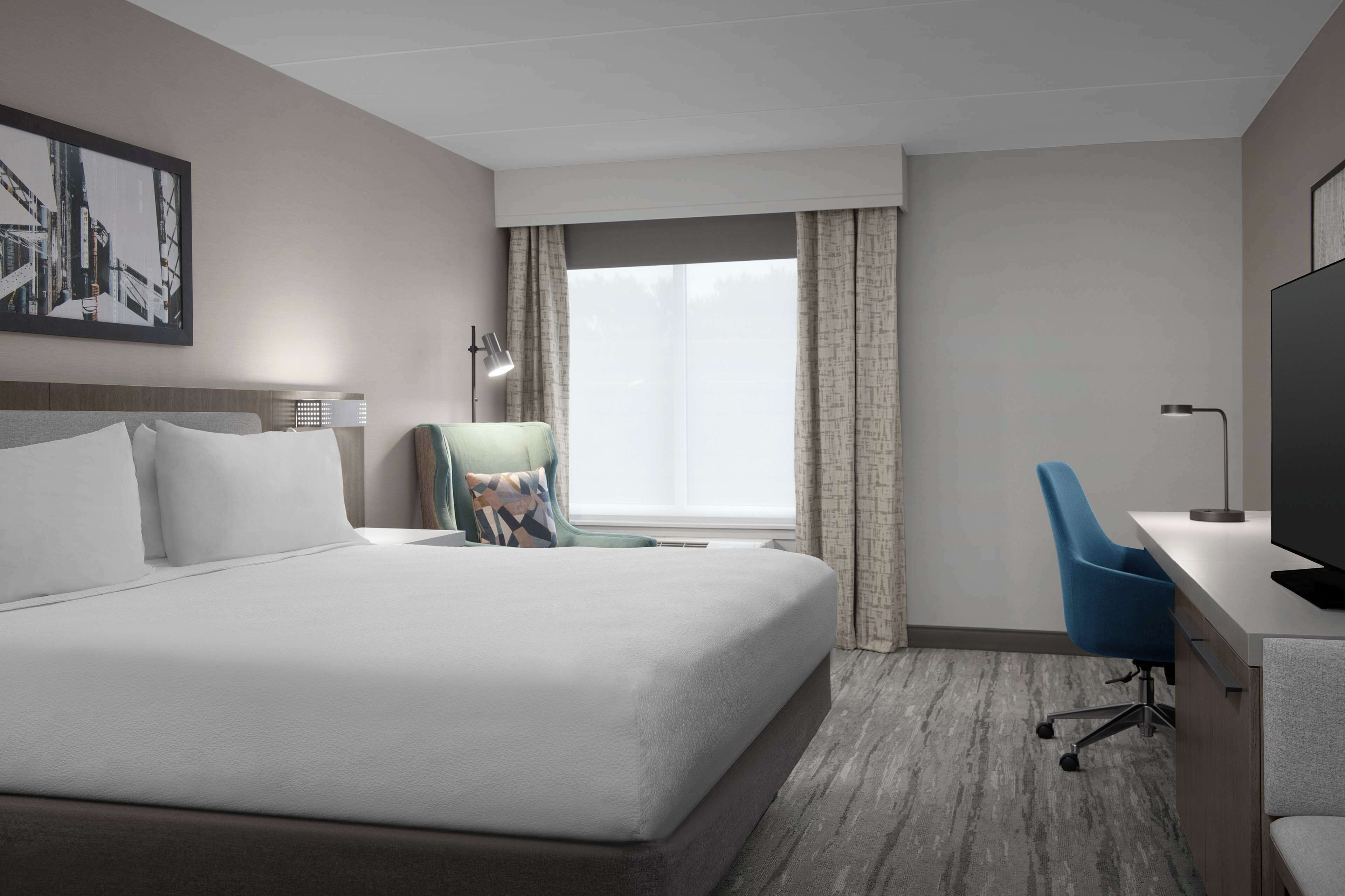 A hotel room with a large bed, a desk with a chair, a TV, and a window with curtains.