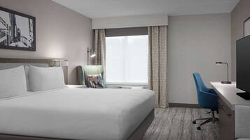 A hotel room with a large bed, a desk with a chair, a TV, and a window with curtains.