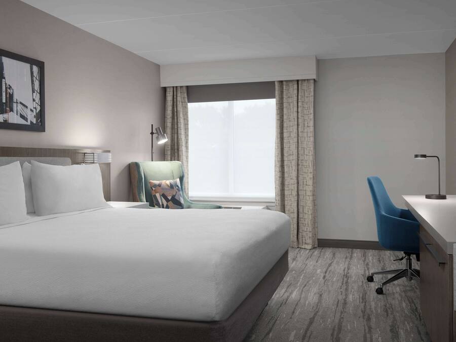 A hotel room with a large bed, a desk with a chair, a TV, and a window with curtains.