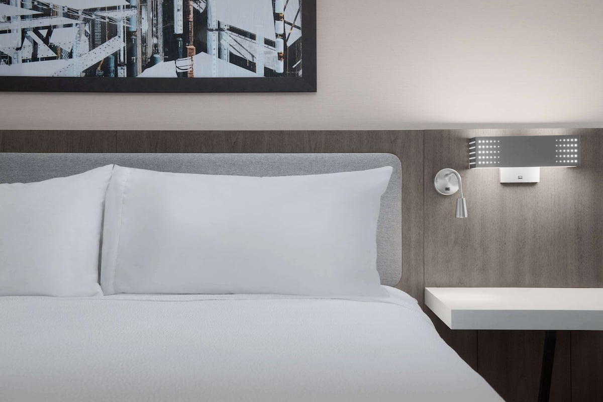 Ein Hotelzimmer mit Bett, Nachttisch, Wandlampe und einem gerahmten Bild über dem Bett.