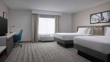 Habitación de hotel con dos camas, un escritorio con silla, un televisor y un amplio ventanal con cortinas.