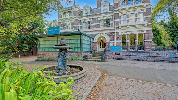 Un edificio histórico con una entrada destacada, una fuente y un cartel que indica que es el Liverpool Aigburch Hotel.