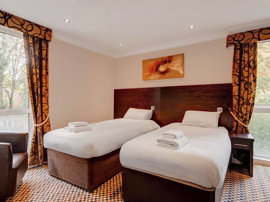 A hotel room with two beds, a wooden headboard, a painting, and a view of trees through the window.