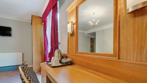 Habitación de hotel con cómoda de madera, un espejo, una araña y una bandeja con hervidor y tazas.