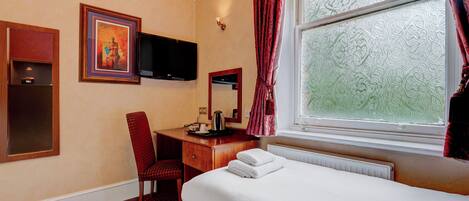 Habitación de hotel con cama, escritorio con silla, televisor, ventana con cortinas y un cuadro en la pared.