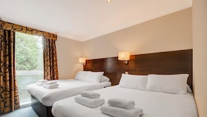 Habitación de hotel con dos camas, cada una con ropa blanca y toallas, cabeceros de madera y una ventana con cortinas.