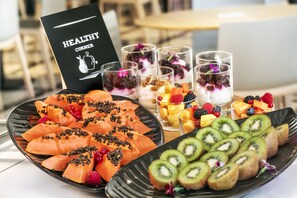 En buffé med skivad frukt och desserter, inklusive kiwi, jordgubbar och ett urval av andra frukter, samt en skylt med texten ”HÄLSOHÖRNET”.