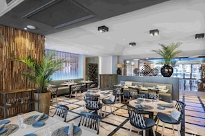 A restaurant with multiple tables and chairs, a wooden wall, and a large potted plant.