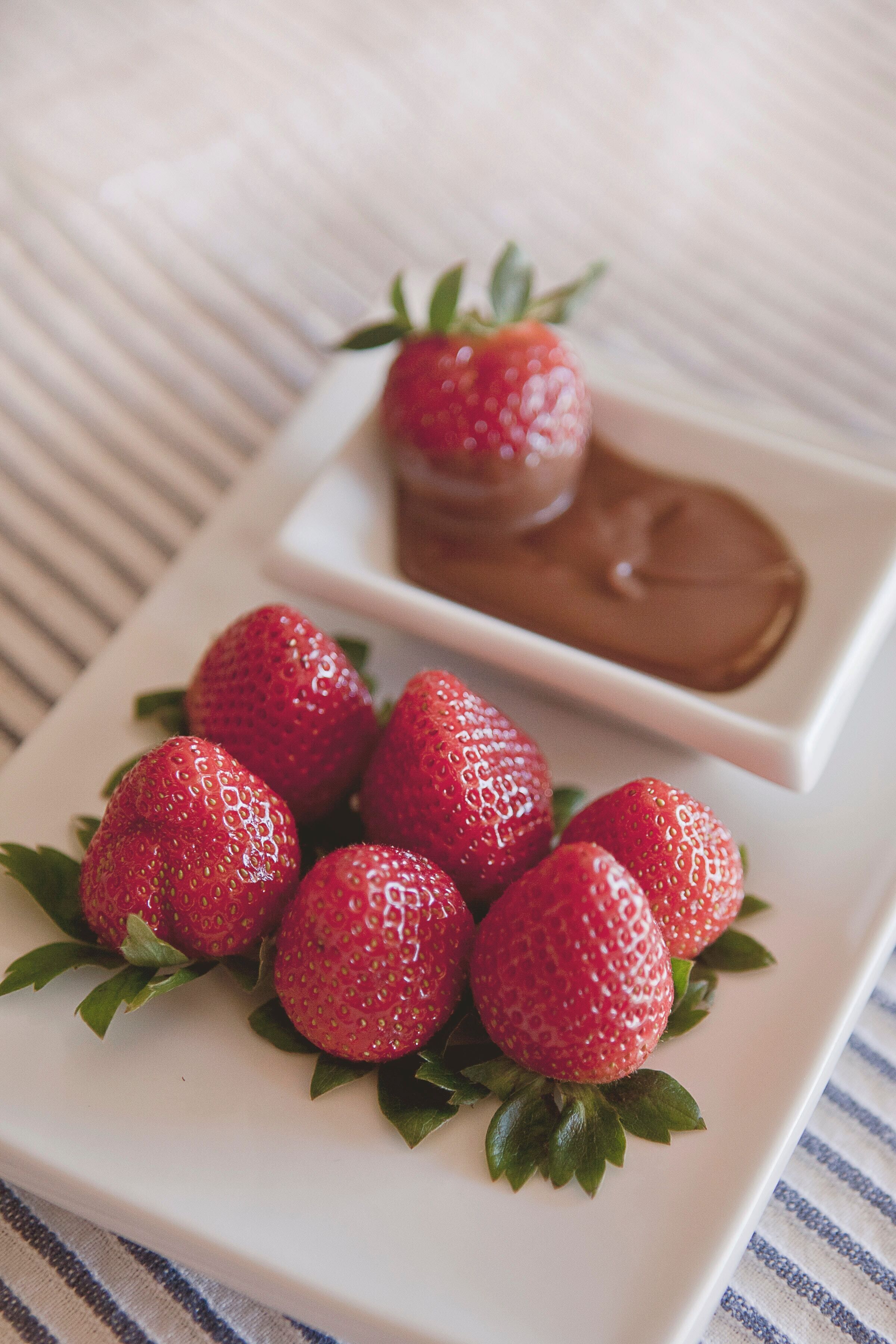 A white plate with six strawberries and a small square dish of chocolate spread.