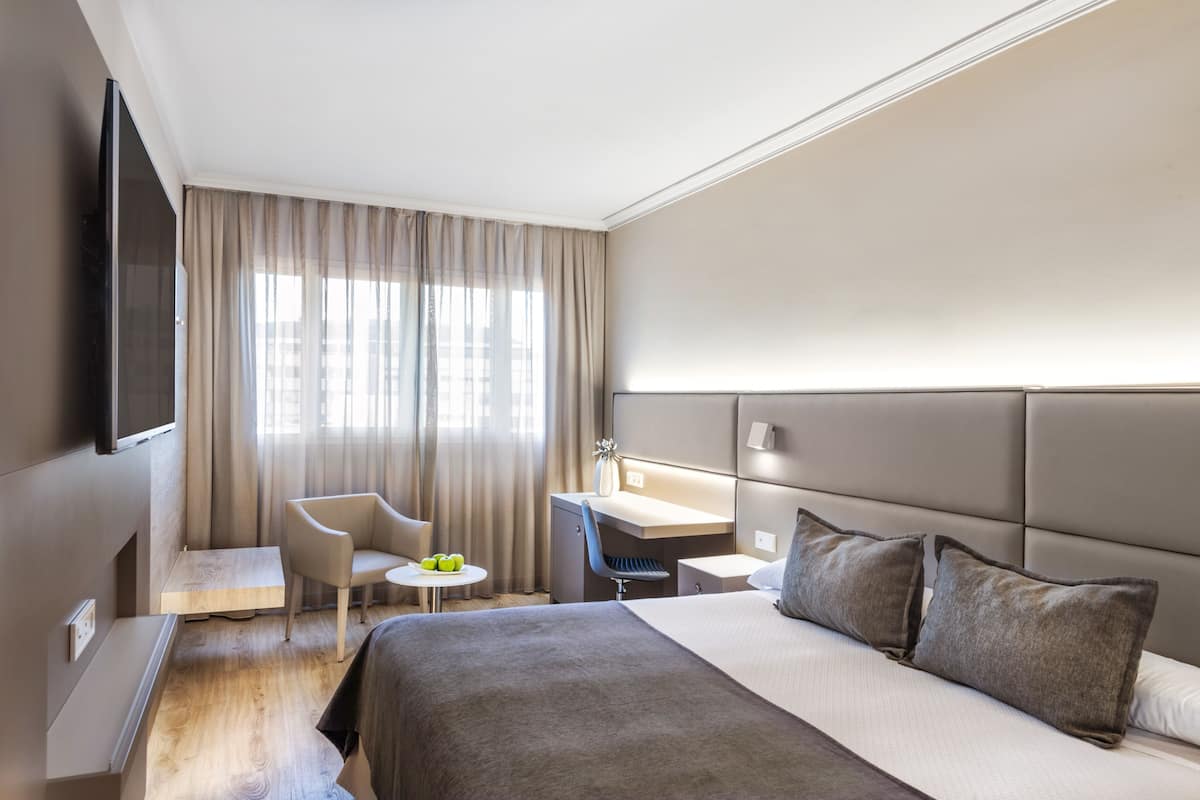 A modern hotel room with a large bed, a desk, a chair, and a television.