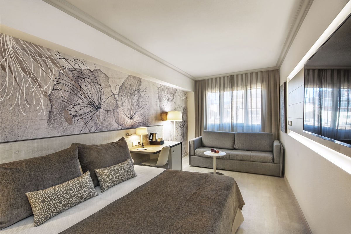 A hotel room with a large bed, a sofa, a desk, and a large abstract painting on the wall.