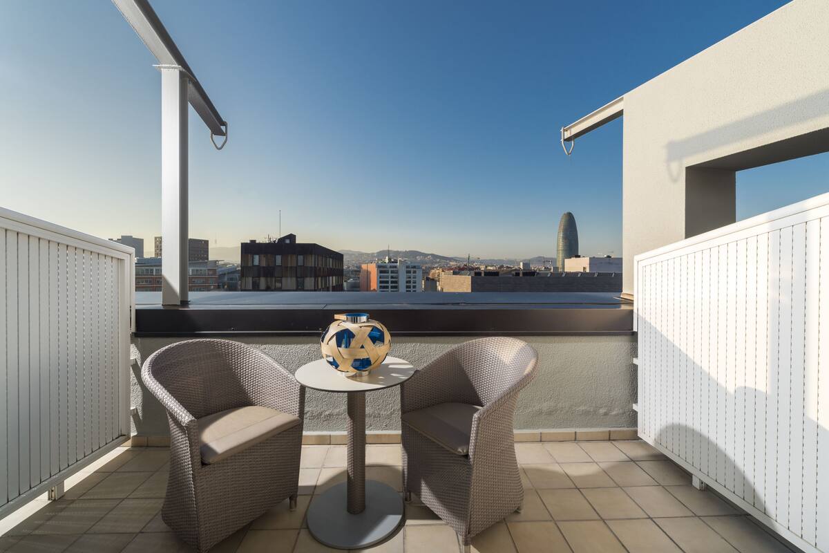 A balcony with two wicker chairs, a small round table, and a decorative soccer ball.