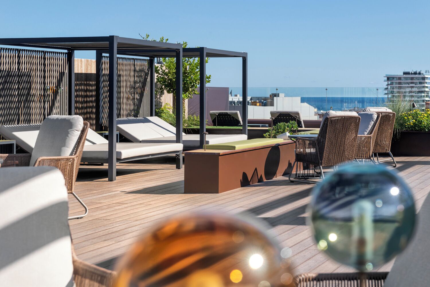 Un salon sur le toit, doté de chaises longues, d’une table à plateau en verre et offrant une vue sur l’océan et les bâtiments.