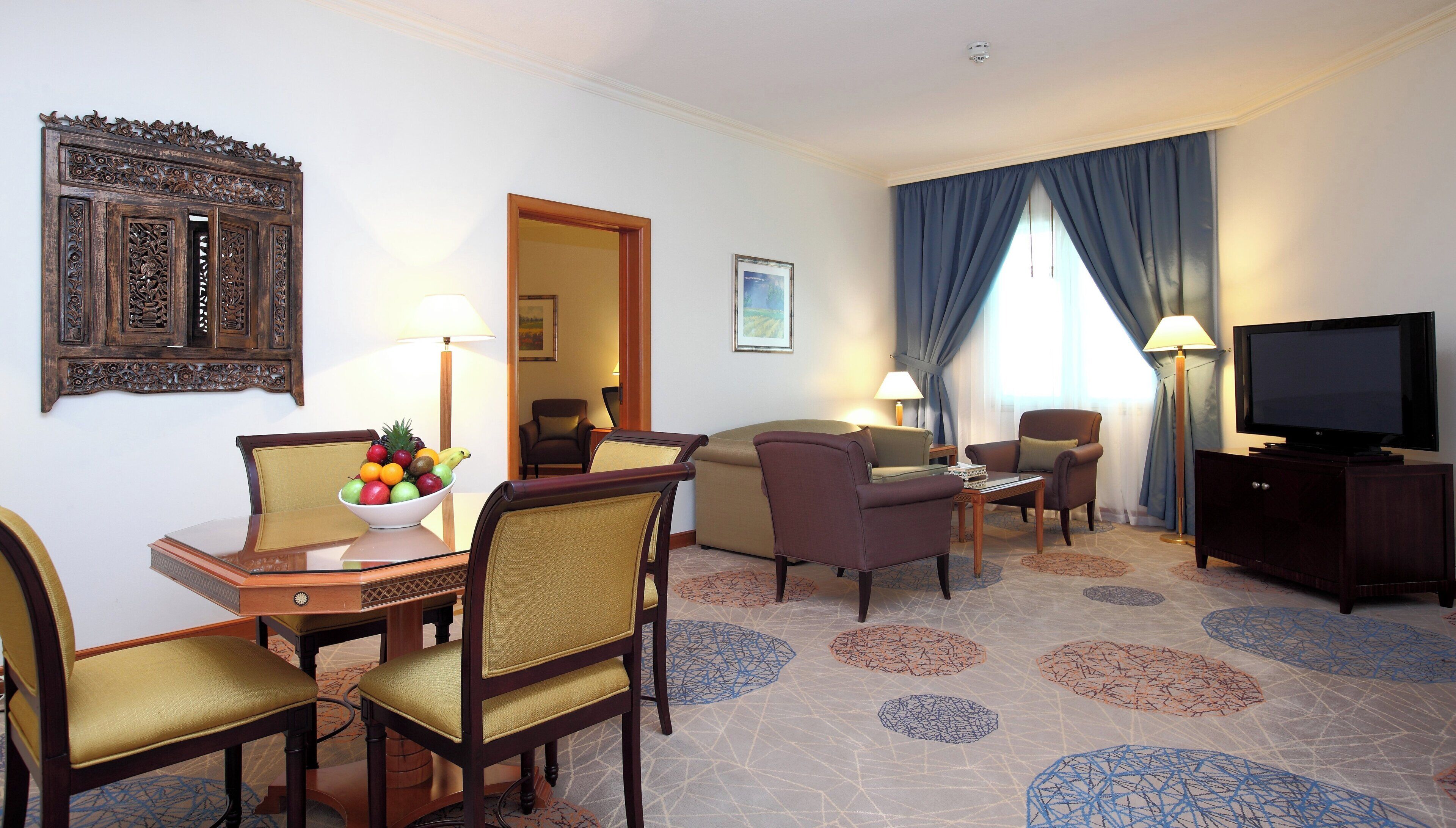 A hotel room with a dining table, chairs, a television, a sofa, and a decorative wall piece.