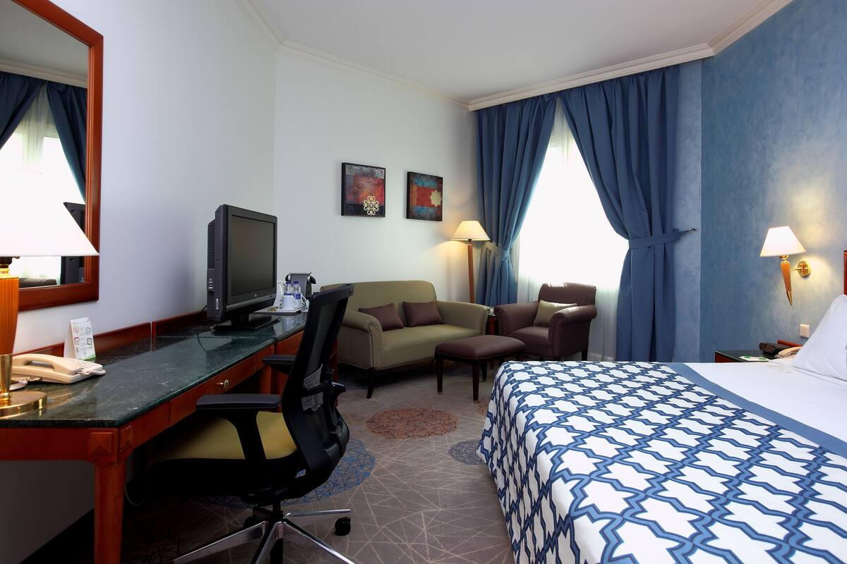 A hotel room with a bed, desk, office chair, two armchairs, a television, lamps, and a coffee maker.