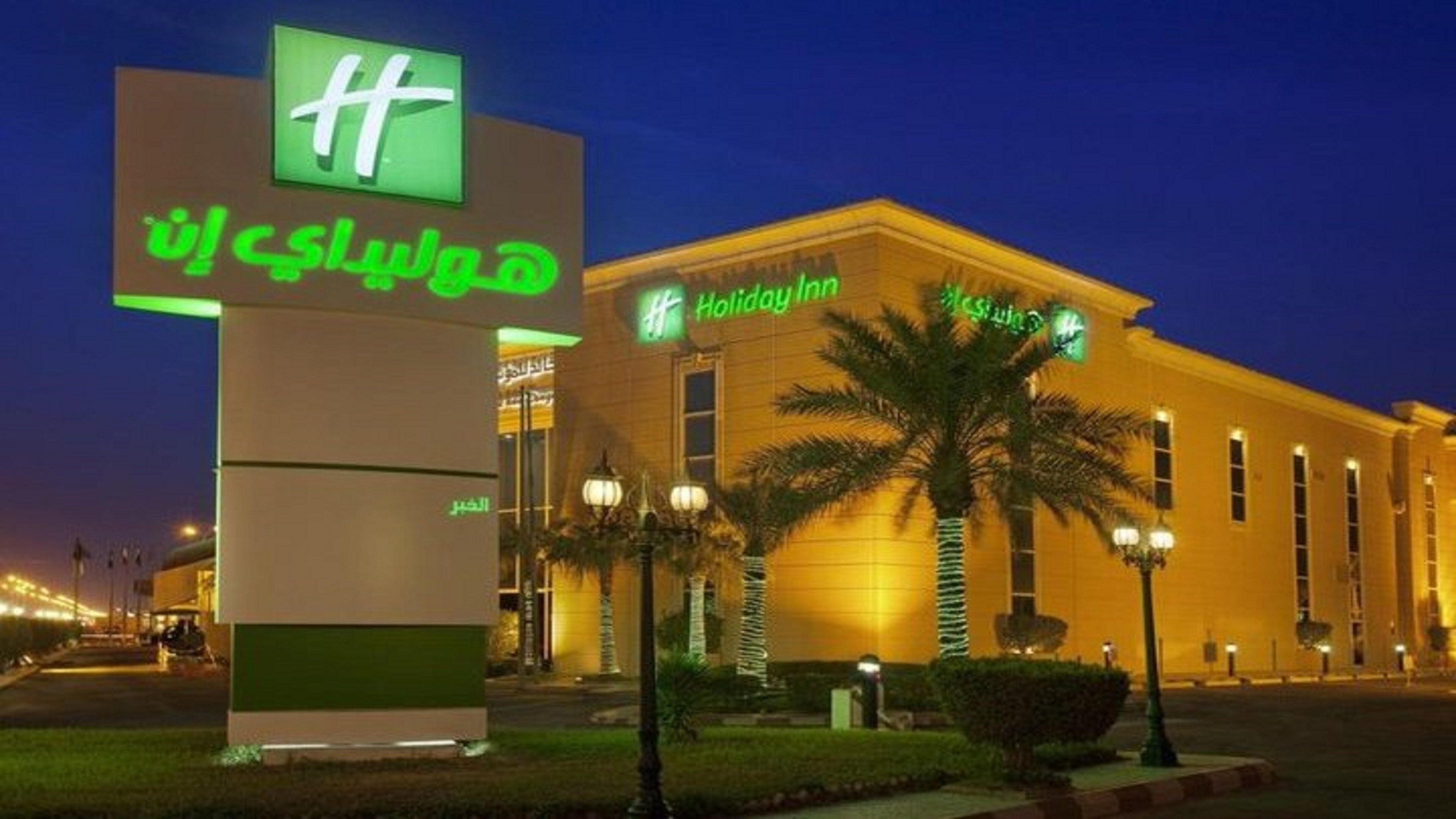 Un hotel Holiday Inn Express con un letrero llamativo, palmeras y una fachada bien iluminada.