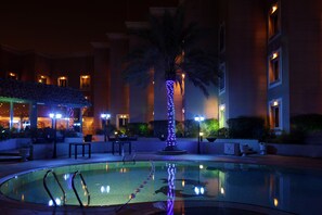 A pool area with a palm tree, lounge chairs, and a building in the background. - Holiday Inn Al Khobar by IHG (Al Khobar)