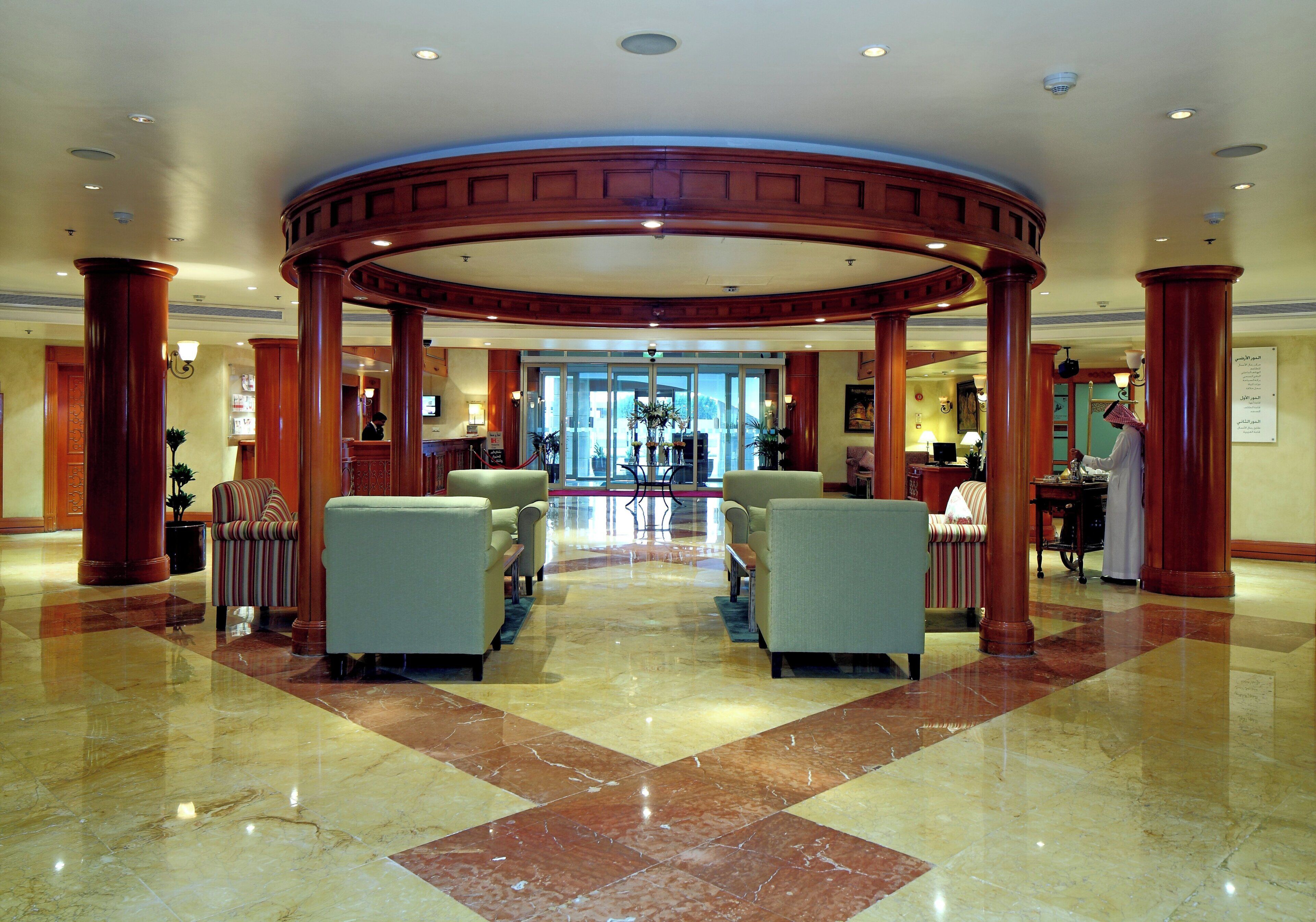 Um hall com estrutura de coluna circular, áreas de estar e balcão de recepção.
