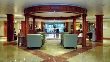 Um hall com estrutura de coluna circular, áreas de estar e balcão de recepção.