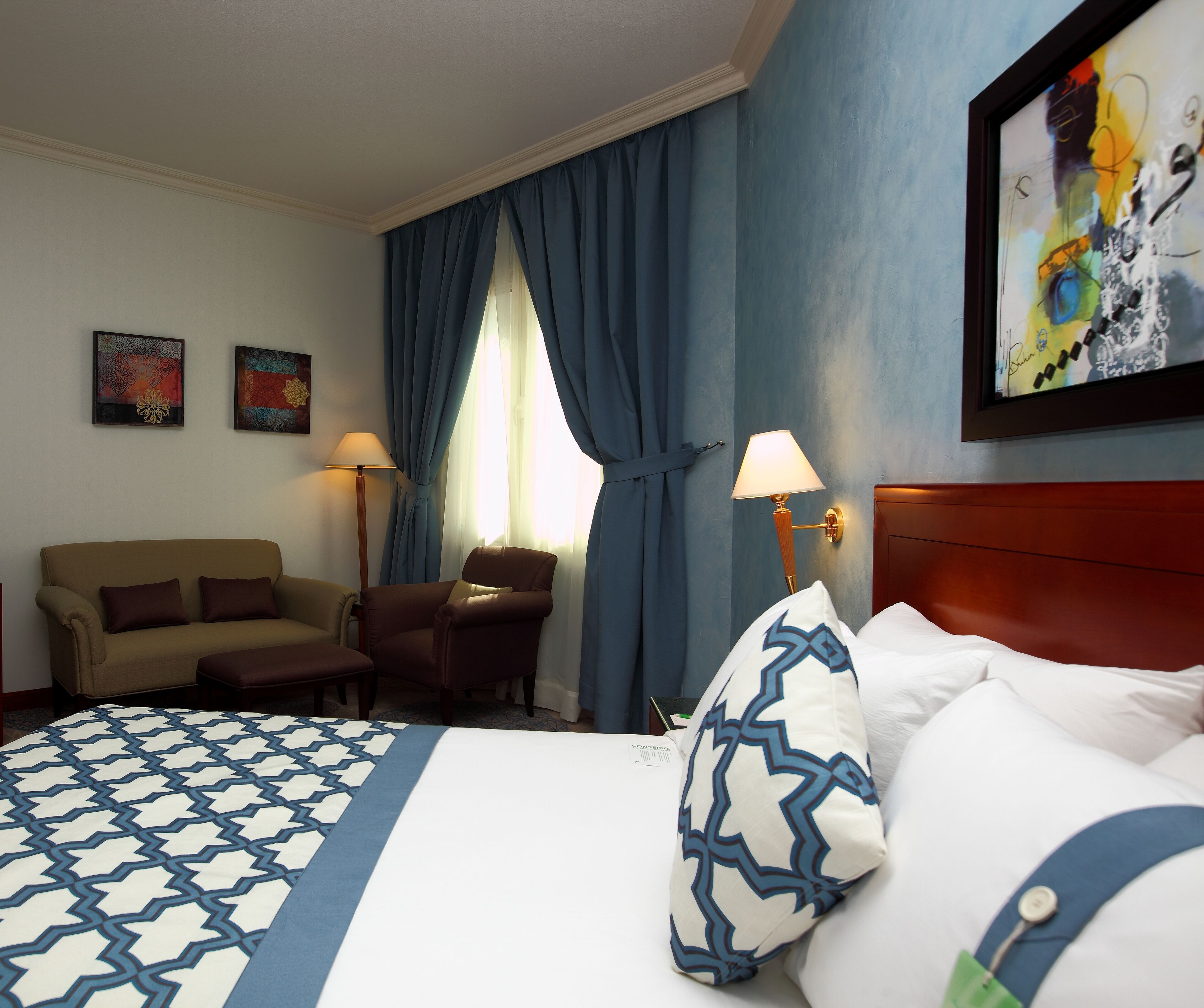 Una habitación de hotel con cama, sofá, sillón, escritorio y lámpara.