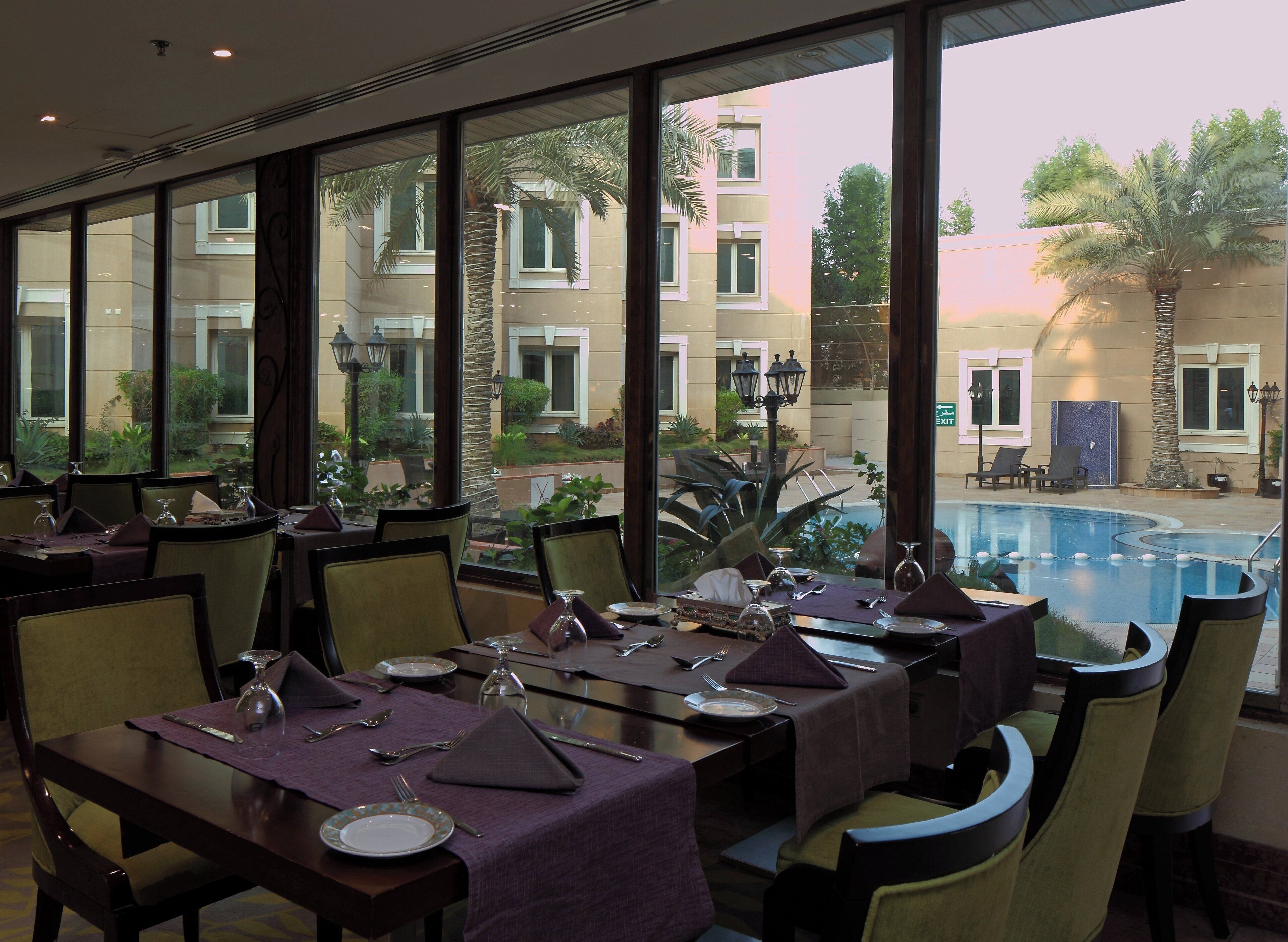 A dining area with tables set for a meal, overlooking a swimming pool and a landscaped garden.