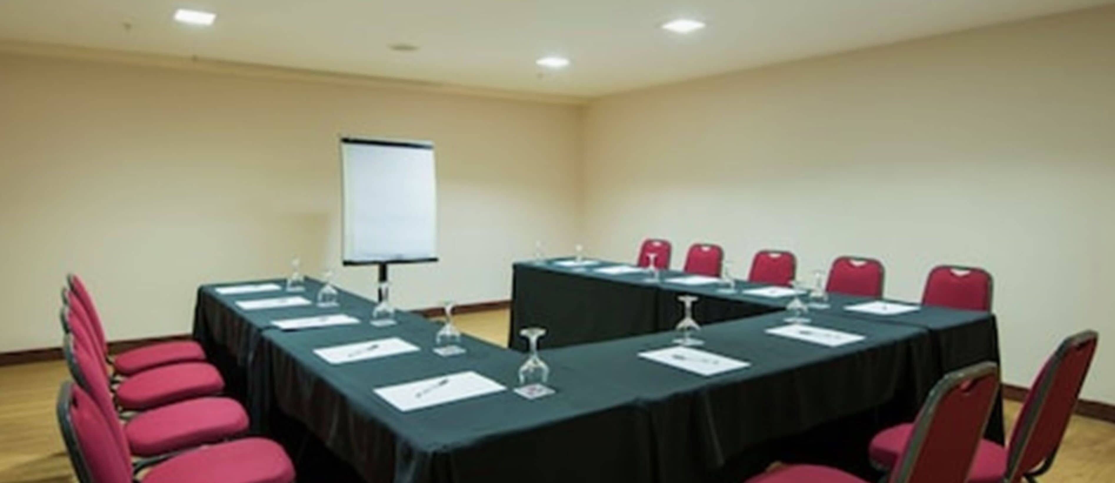 A conference room with a long table, red chairs, a projector screen, and a whiteboard.