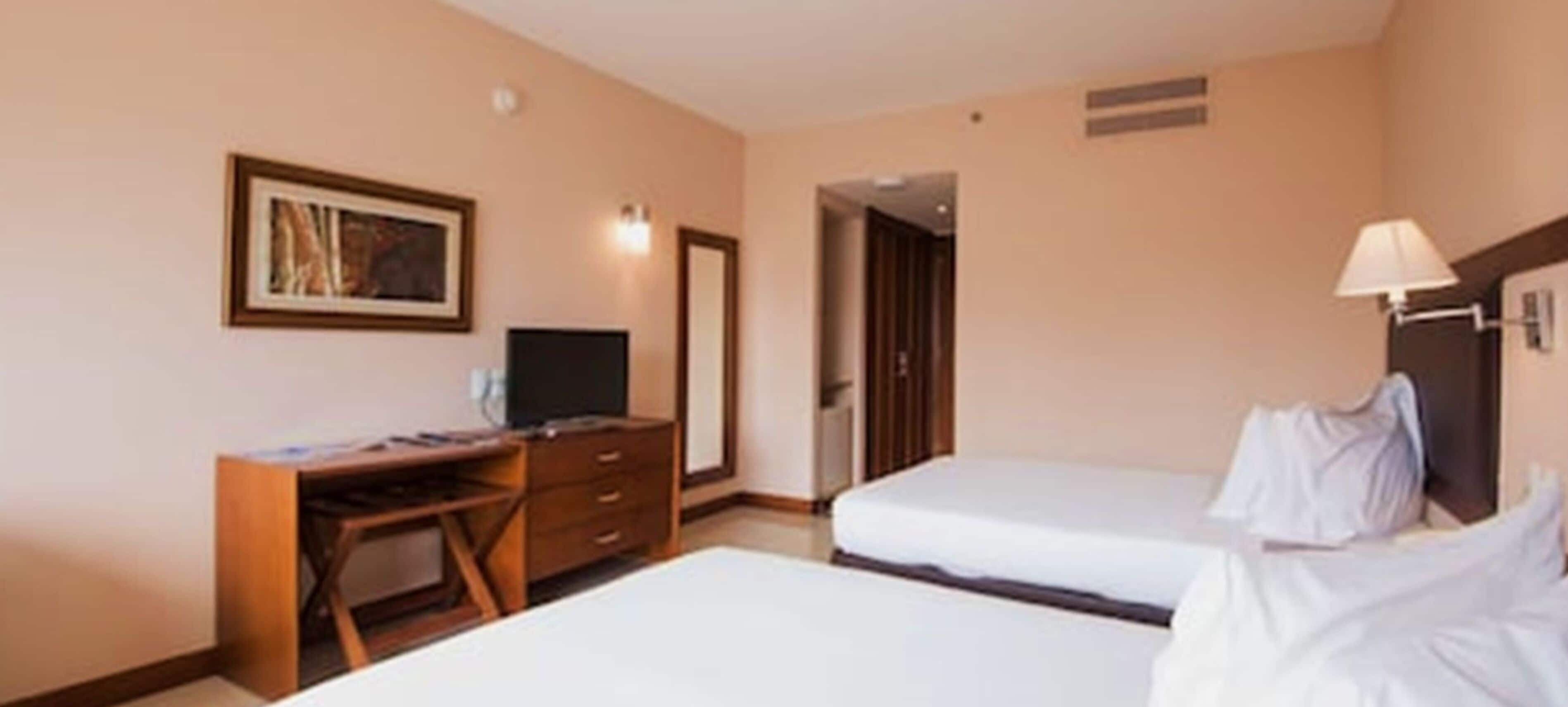 Una camera d'albergo con due letti, una scrivania, una televisione e un quadro appeso al muro.