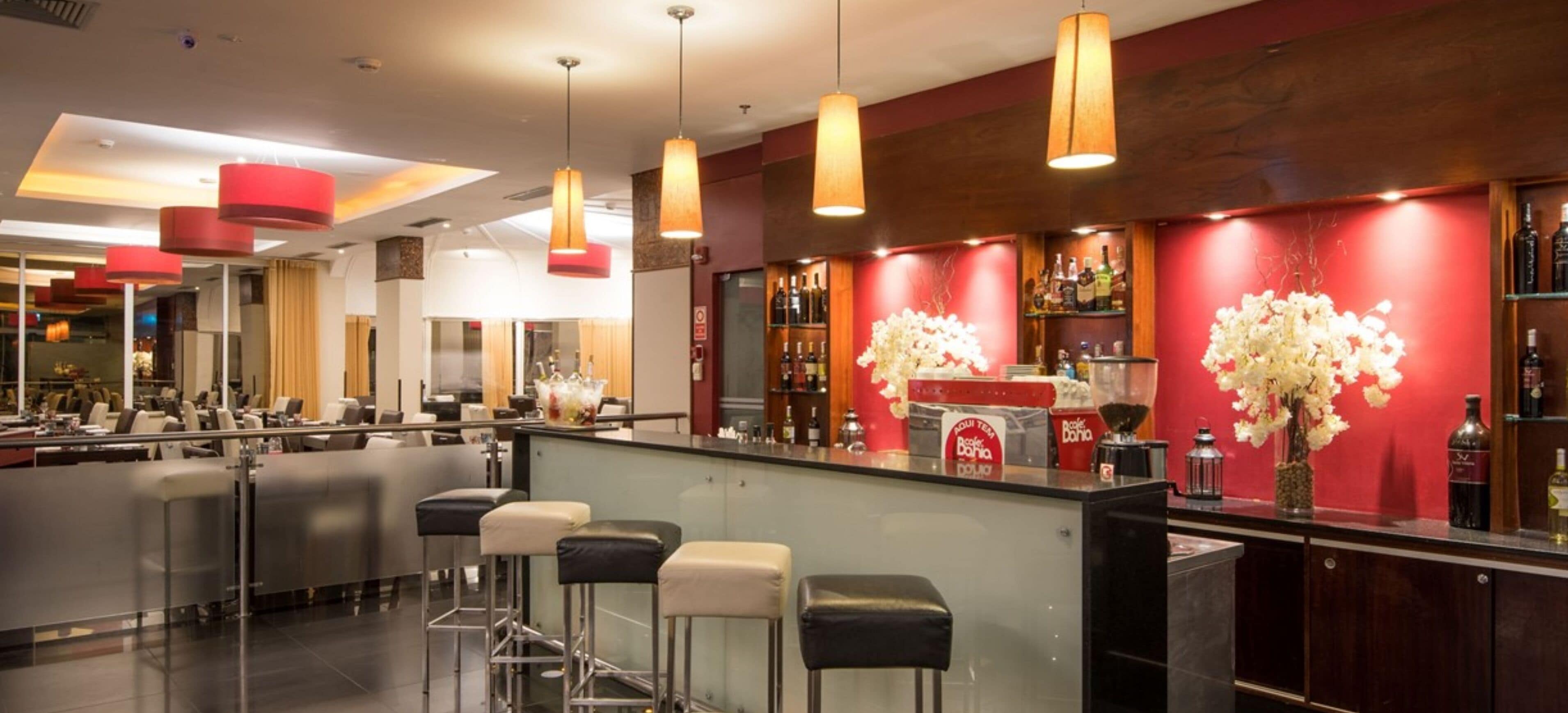 Uma área de bar moderna com balcão, banquetas e luminárias pendentes.