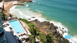 Vista da piscina com águas cristalinas, praia de areia e costa rochosa.