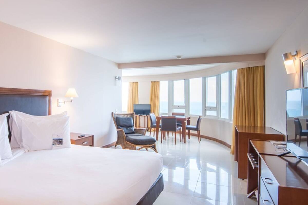 Ein Hotelzimmer mit einem großen Bett, einem Schreibtisch, einem Stuhl, einem Fernseher und einem Fenster mit Vorhängen.