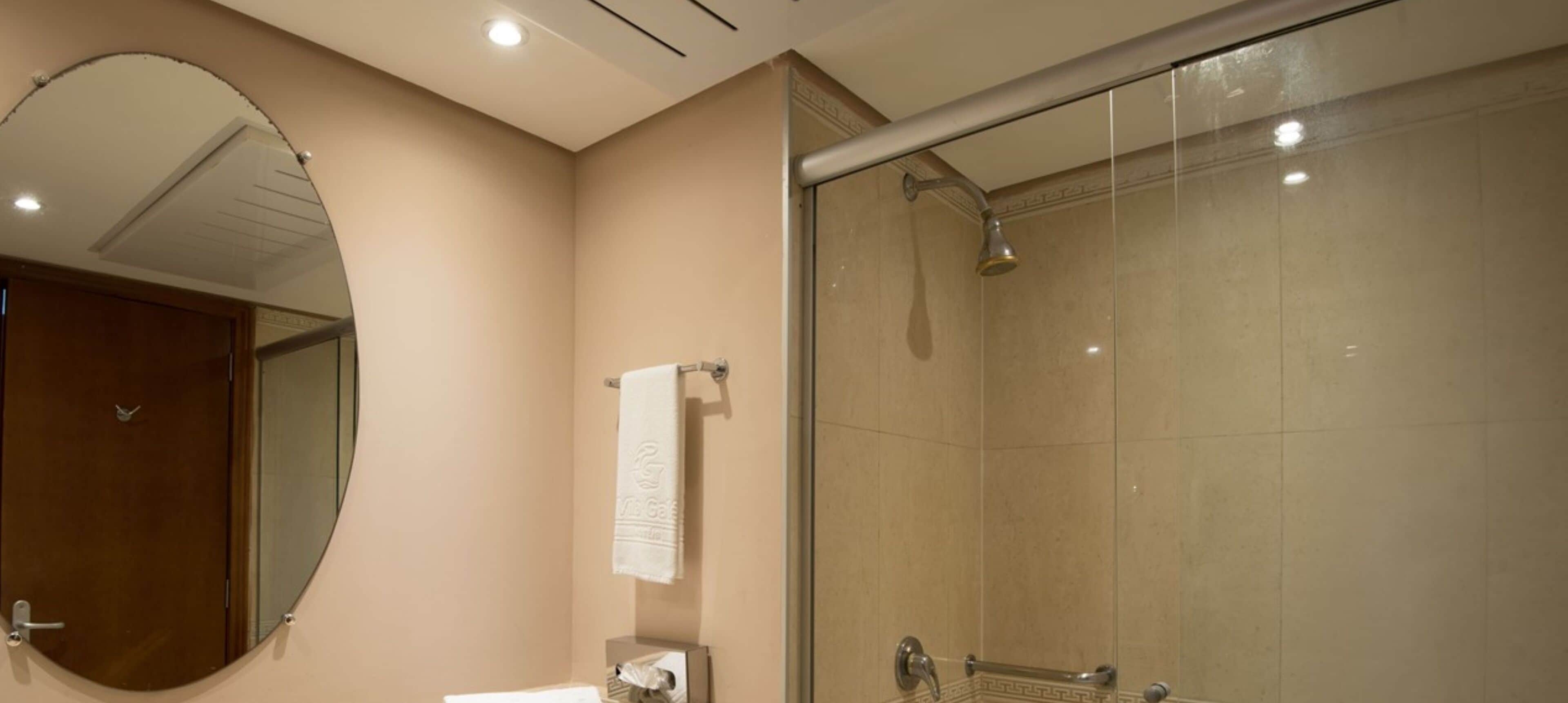 A bathroom with a glass-enclosed shower, a round mirror, and a towel rack.