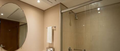 A bathroom with a glass-enclosed shower, a round mirror, and a towel rack.
