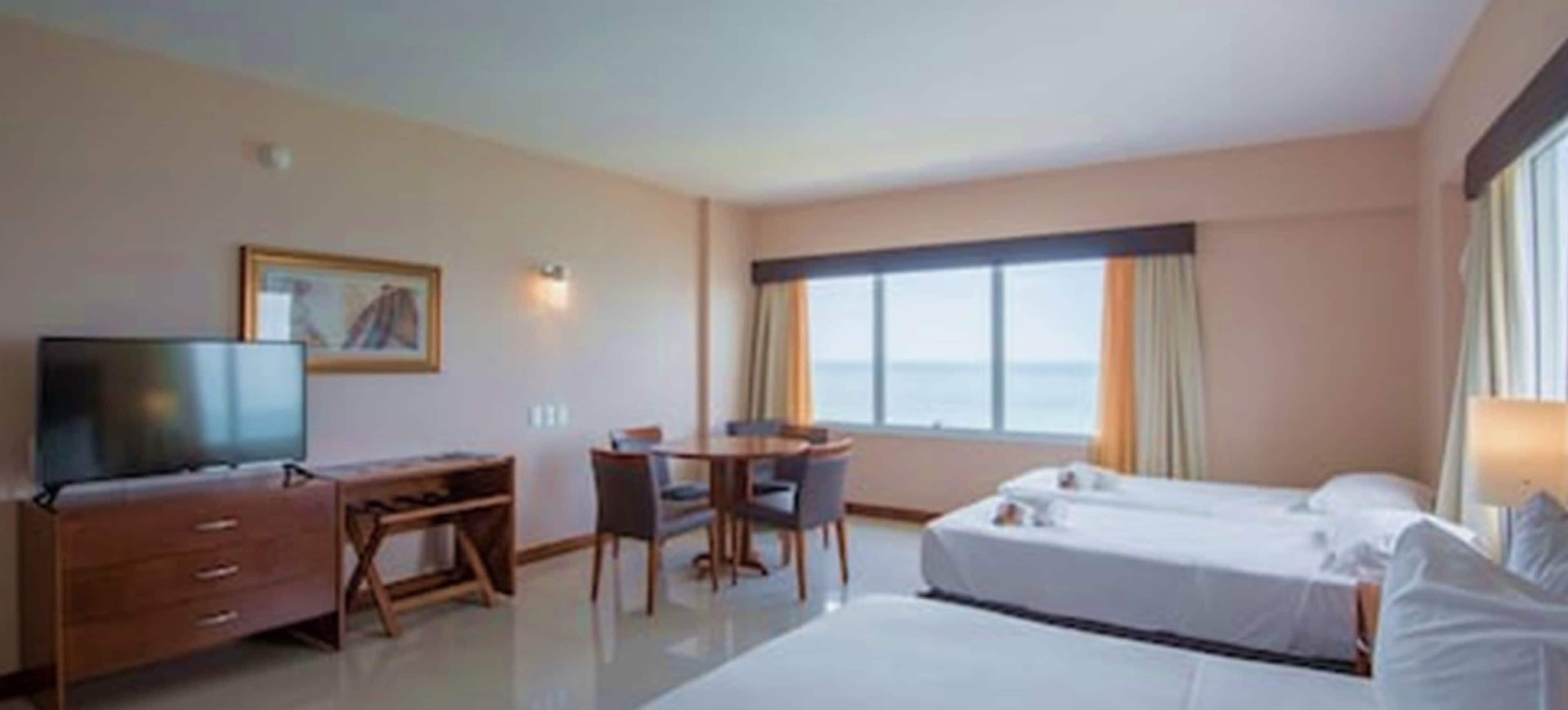 A hotel room with two beds, a desk, a chair, a television, and a large window with curtains.