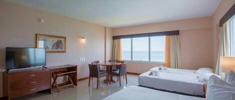 A hotel room with two beds, a desk, a chair, a television, and a large window with curtains.