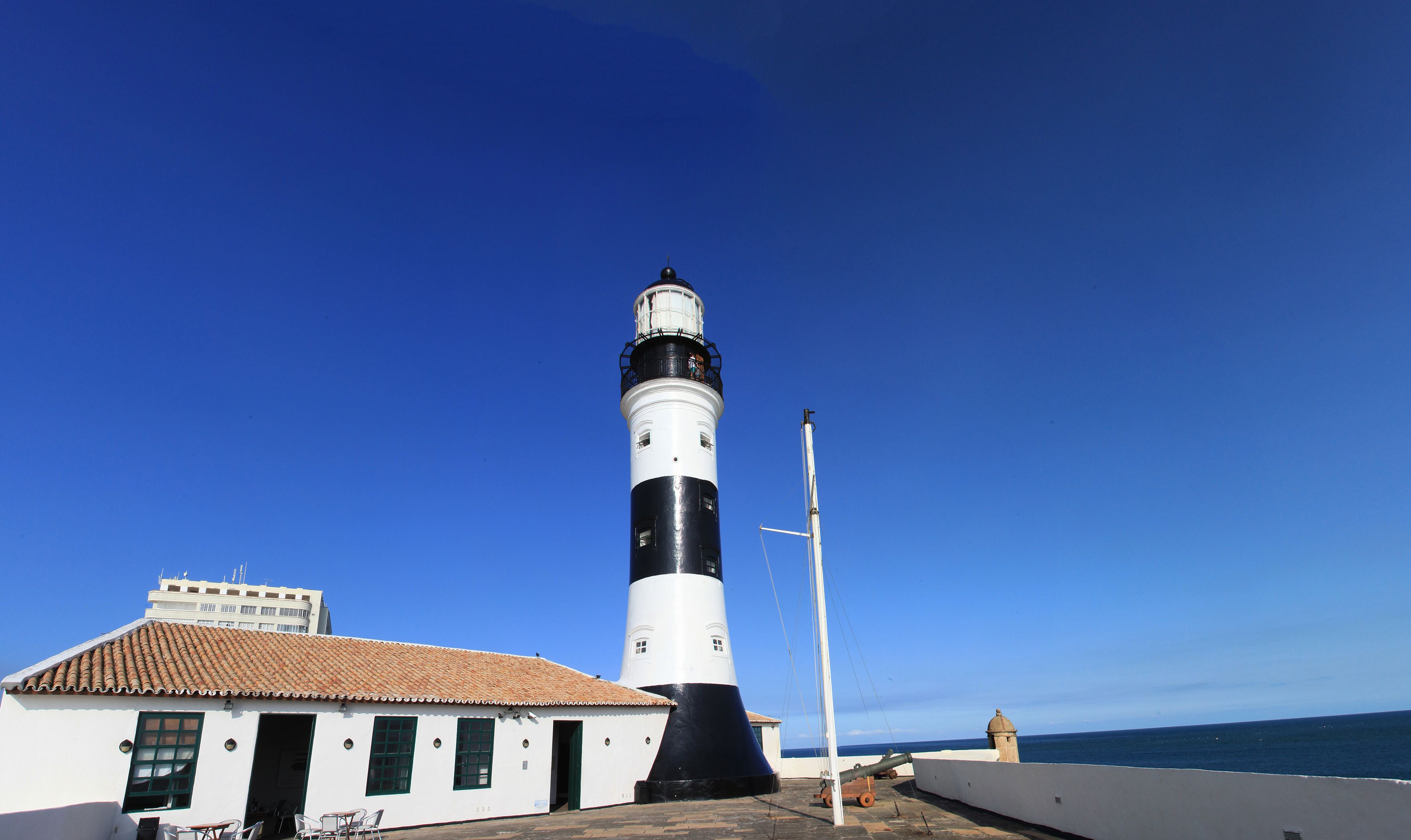 A lighthouse with a white and black exterior, a tiled roof, and a small adjacent building with a tiled roof and a door.