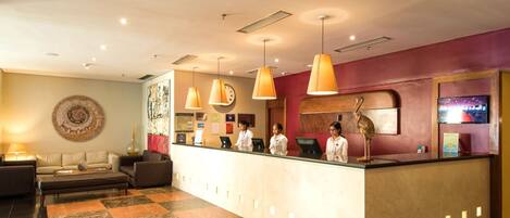 A hotel reception area with a reception desk, three staff members, a clock, and a large wall clock.
