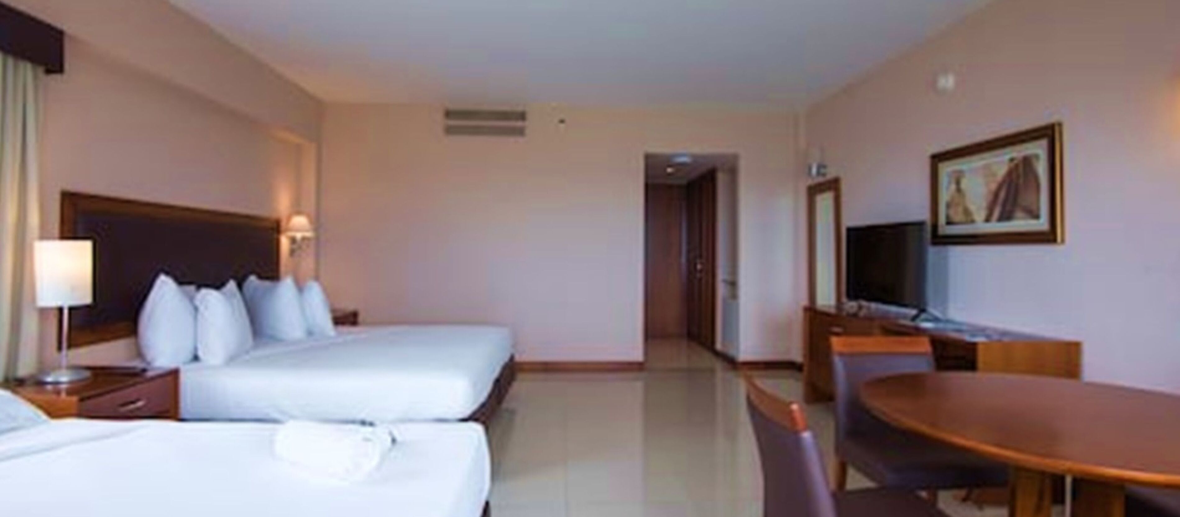 A hotel room with two beds, a desk, a chair, a television, and a painting on the wall.