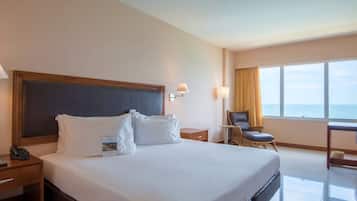 Een hotelkamer met een groot bed, een bureau met stoel, een lamp en uitzicht op de oceaan.